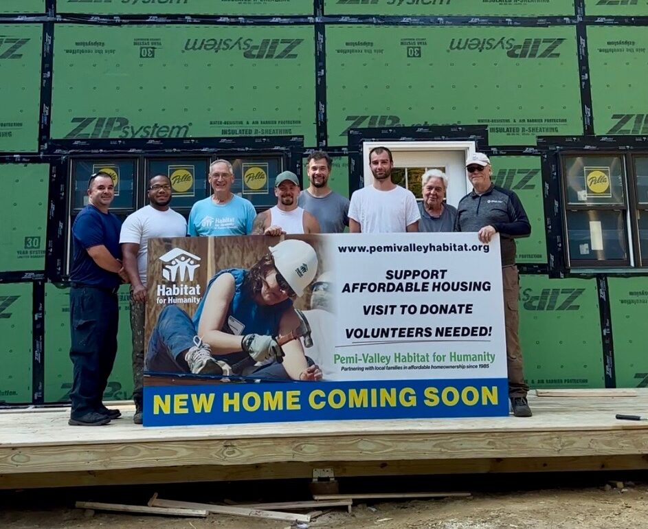 A group of Habitat for Humanity workers holding up a new home coming soon sign.